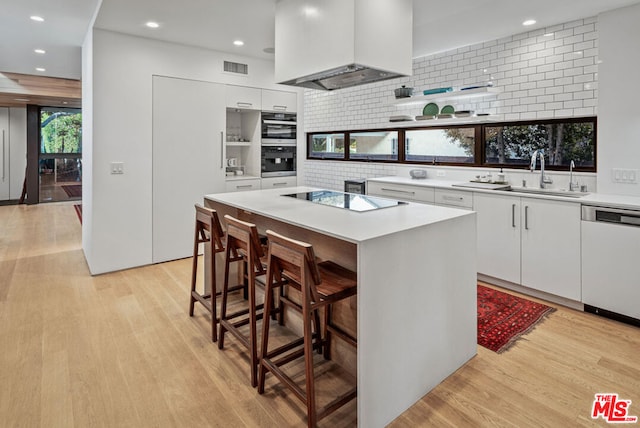 kitchen featuring custom exhaust hood, a center island, appliances with stainless steel finishes, light hardwood / wood-style floors, and white cabinetry