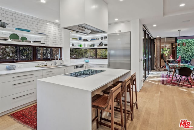 kitchen with custom exhaust hood, black electric cooktop, light hardwood / wood-style flooring, white cabinets, and built in refrigerator