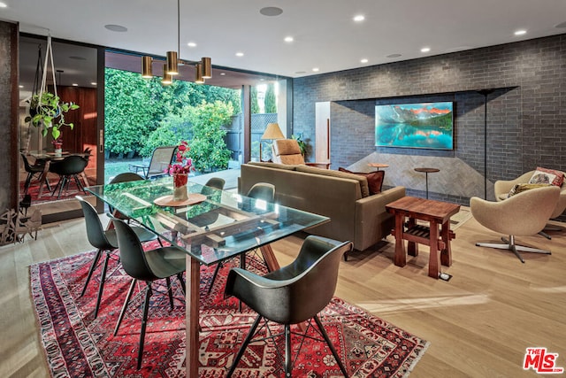 dining area featuring wood-type flooring, brick wall, and a wall of windows