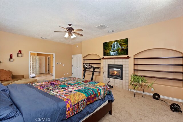 carpeted bedroom featuring ceiling fan, a tile fireplace, and a textured ceiling