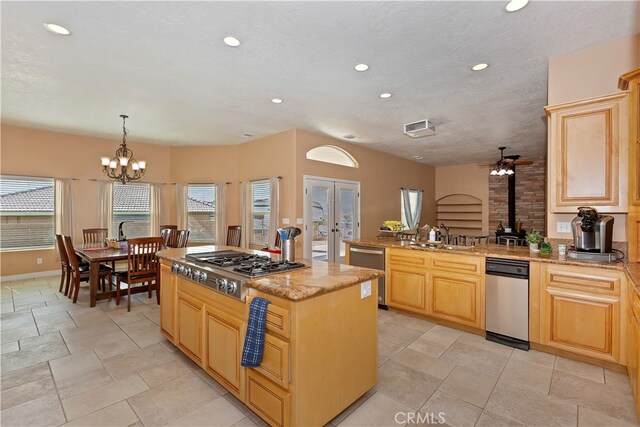 kitchen featuring ceiling fan with notable chandelier, pendant lighting, a wood stove, a center island, and light brown cabinetry