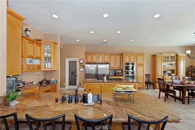 kitchen with light tile patterned floors, kitchen peninsula, stainless steel appliances, a breakfast bar, and an inviting chandelier