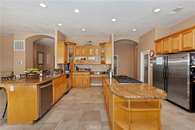 kitchen with a textured ceiling, kitchen peninsula, a kitchen breakfast bar, stainless steel appliances, and light stone countertops