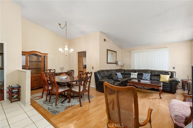 dining room featuring lofted ceiling, light wood finished floors, a textured ceiling, and a chandelier