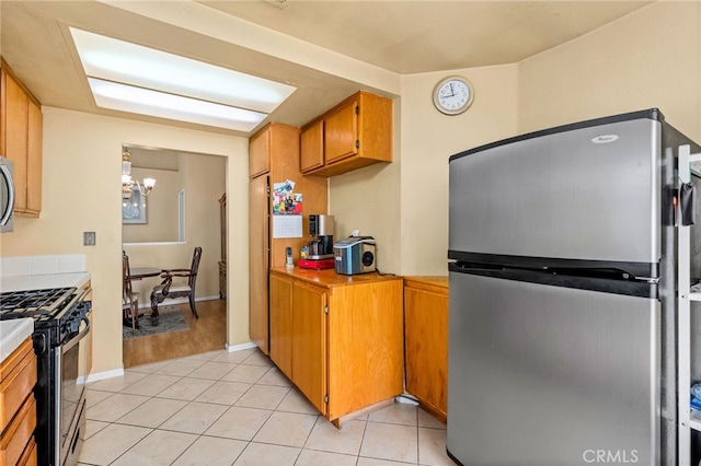 kitchen featuring light tile patterned floors, stainless steel appliances, light countertops, brown cabinets, and an inviting chandelier