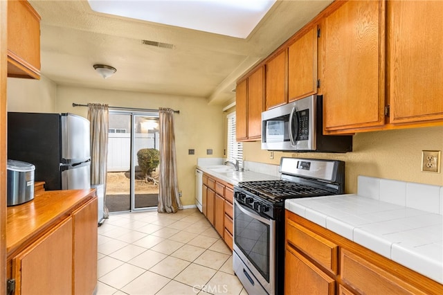 kitchen with light tile patterned floors, tile counters, visible vents, appliances with stainless steel finishes, and a sink