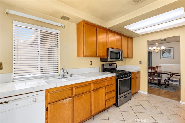 kitchen featuring tile countertops, light tile patterned flooring, stainless steel appliances, a sink, and an inviting chandelier