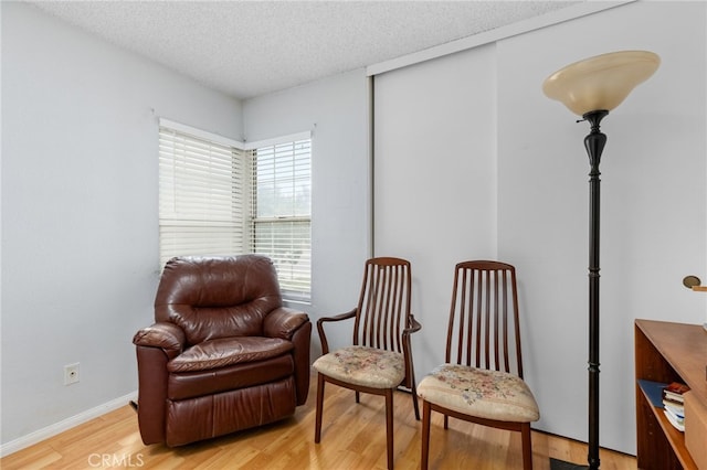 living area with light wood-type flooring, a textured ceiling, and baseboards