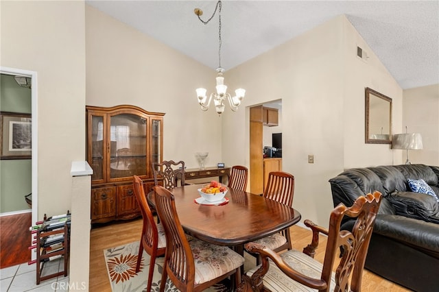 dining space featuring a textured ceiling, a notable chandelier, visible vents, vaulted ceiling, and light wood-type flooring