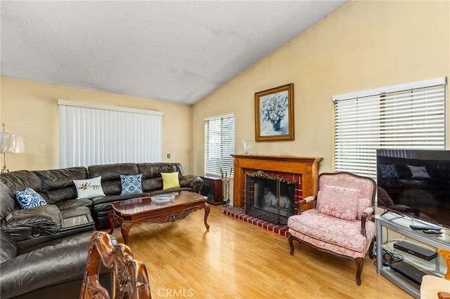 living room featuring vaulted ceiling, a textured ceiling, a brick fireplace, and wood finished floors