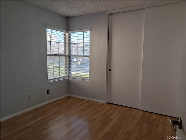 unfurnished room with a textured ceiling, light wood-type flooring, a wealth of natural light, and baseboards