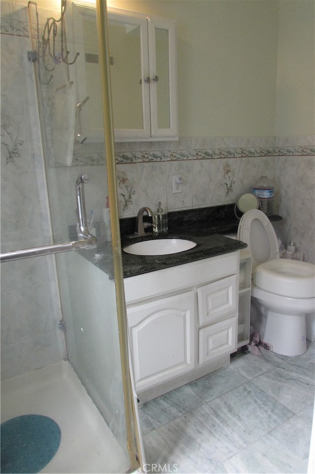 bathroom with vanity, tile walls, a tile shower, and toilet