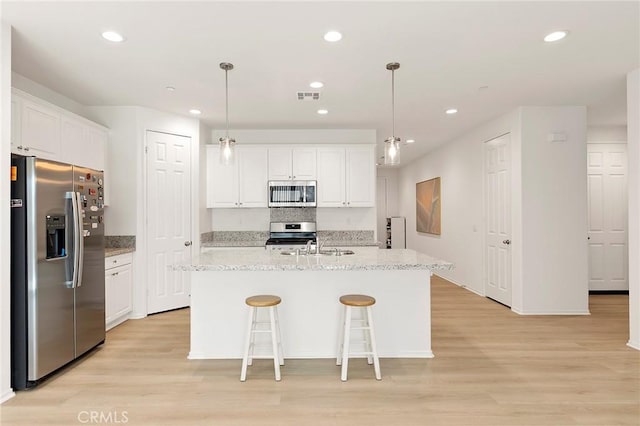 kitchen with an island with sink, stainless steel appliances, white cabinetry, and light hardwood / wood-style flooring