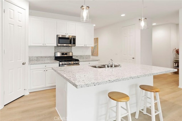 kitchen featuring stainless steel appliances, an island with sink, decorative light fixtures, white cabinets, and light wood-type flooring