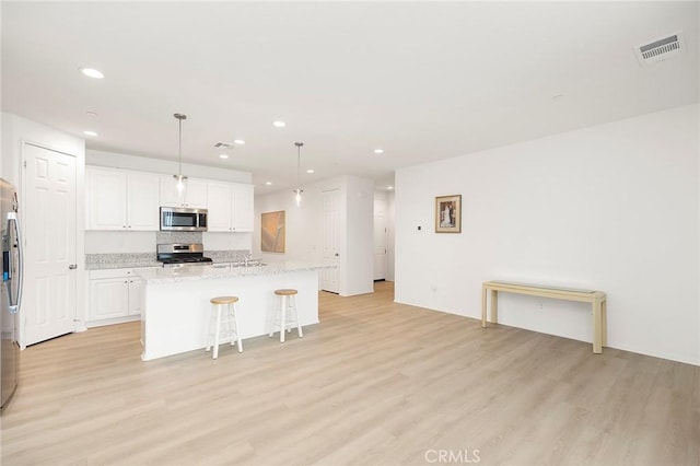 kitchen with decorative light fixtures, stainless steel appliances, light hardwood / wood-style floors, and an island with sink