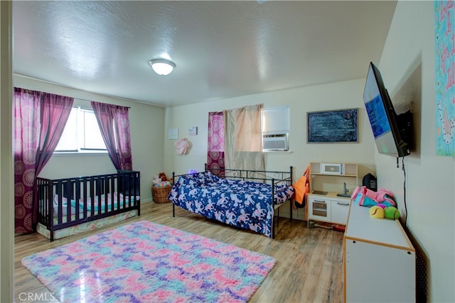 bedroom featuring cooling unit, a textured ceiling, and light hardwood / wood-style flooring