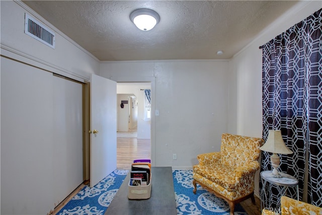 living area with a textured ceiling, ornamental molding, and hardwood / wood-style flooring