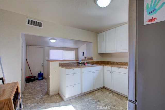 kitchen with stainless steel refrigerator, kitchen peninsula, white cabinetry, and sink