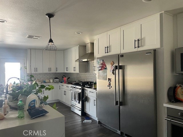 kitchen featuring white cabinets, hanging light fixtures, wall chimney exhaust hood, dark wood-type flooring, and stainless steel appliances