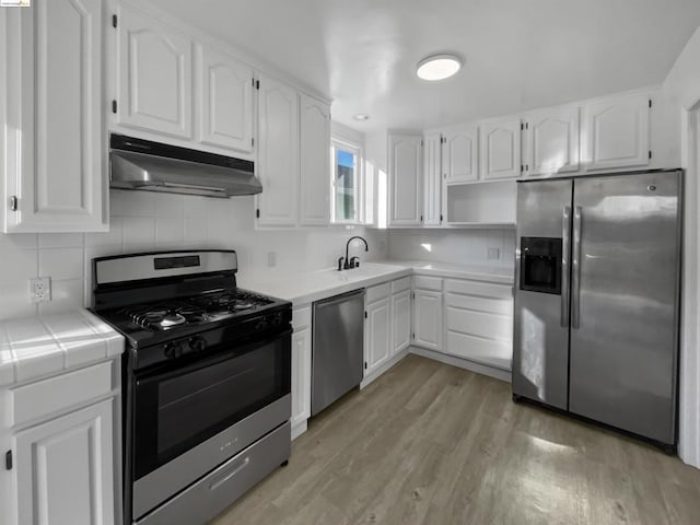 kitchen with stainless steel appliances, sink, tile countertops, light hardwood / wood-style flooring, and white cabinetry