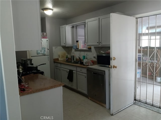 kitchen with white refrigerator, black dishwasher, sink, and light tile patterned flooring