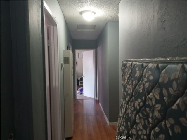 hallway with a textured ceiling and hardwood / wood-style flooring