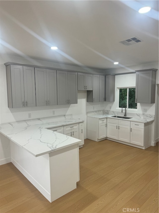 kitchen with light stone countertops, light wood-type flooring, and kitchen peninsula