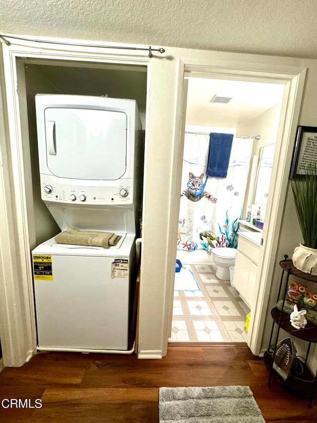 washroom with a textured ceiling, stacked washer / dryer, and dark hardwood / wood-style flooring