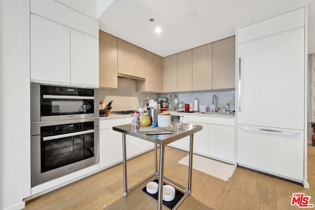 kitchen with sink, stainless steel appliances, exhaust hood, and light hardwood / wood-style floors