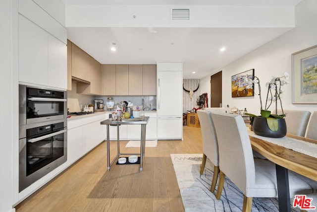 kitchen with appliances with stainless steel finishes, light hardwood / wood-style flooring, decorative backsplash, and white cabinetry