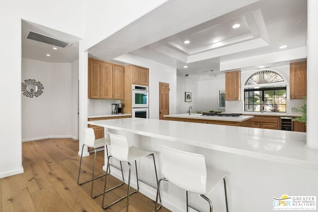 kitchen with beverage cooler, a raised ceiling, light hardwood / wood-style floors, white appliances, and a kitchen island