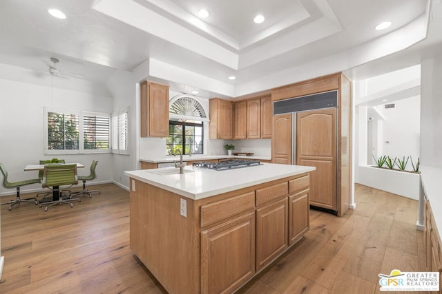 kitchen with sink, paneled fridge, stainless steel gas cooktop, light hardwood / wood-style flooring, and a center island with sink