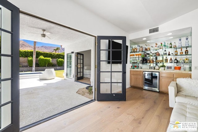 bar with ceiling fan, wine cooler, light hardwood / wood-style floors, lofted ceiling, and light brown cabinetry