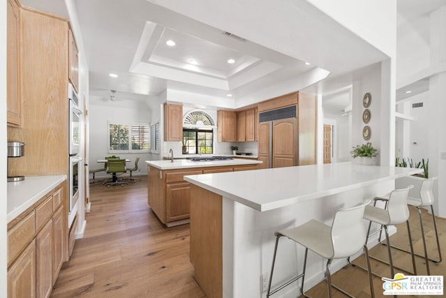 kitchen with a center island, a raised ceiling, paneled fridge, light hardwood / wood-style floors, and a breakfast bar area