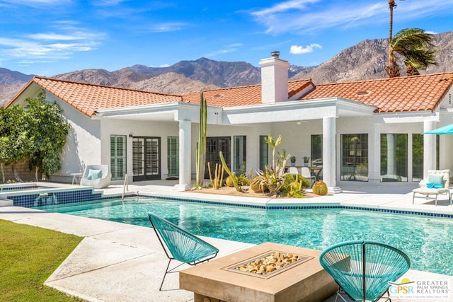 rear view of house with a mountain view, a patio, a fire pit, and a pool with hot tub