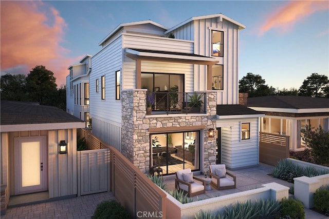 back house at dusk featuring a balcony and a patio