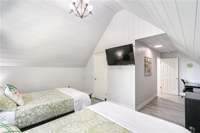 bedroom featuring an inviting chandelier, light hardwood / wood-style flooring, wood walls, and lofted ceiling