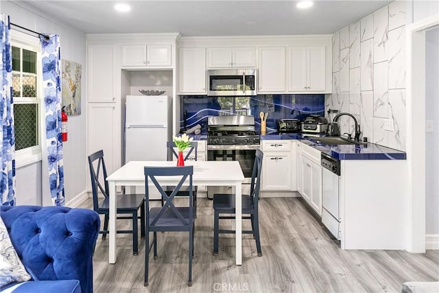 28281 Arbon Ln, Lake Arrowhead, CA 92352 - kitchen with stainless steel appliances, a sink, dark countertops, white cabinets, and light wood-type flooring