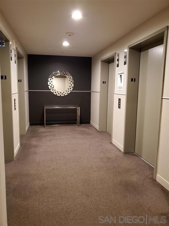 hall with light colored carpet and elevator