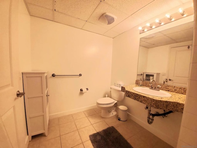 bathroom with a drop ceiling, tile patterned flooring, toilet, and sink