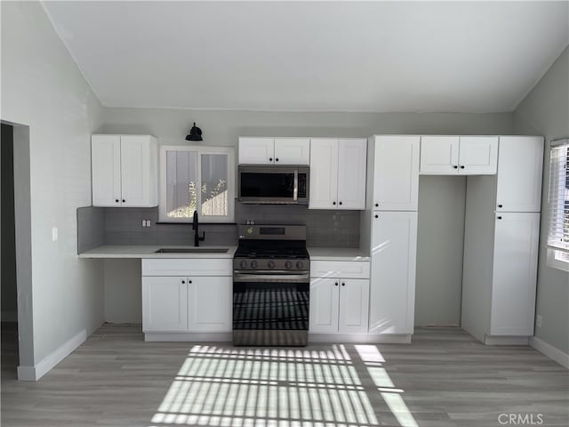 kitchen featuring white cabinets, sink, tasteful backsplash, stainless steel appliances, and light wood-type flooring