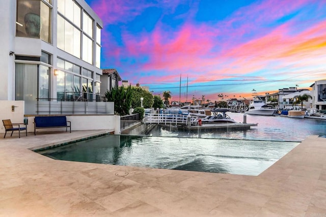 pool at dusk featuring a patio area and a water view