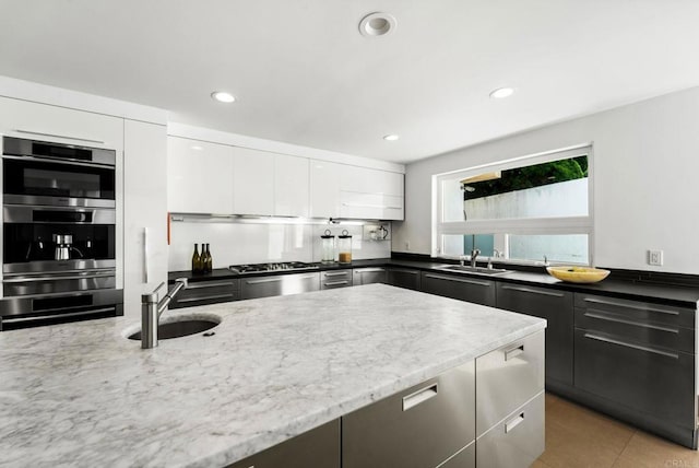 kitchen with light tile patterned flooring, white cabinetry, dark stone countertops, and sink