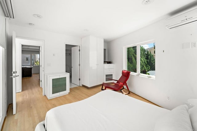 bedroom with light hardwood / wood-style flooring, a wall mounted AC, and multiple windows