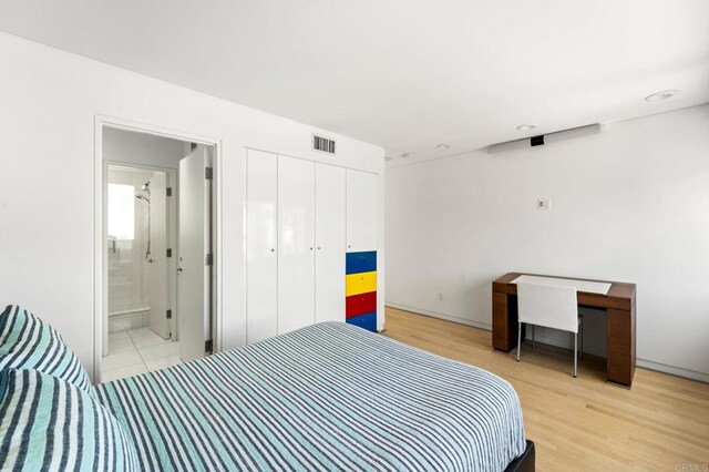 bedroom with ensuite bathroom, light wood-type flooring, and a closet