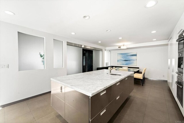 kitchen featuring tile patterned flooring, sink, dark brown cabinetry, and an island with sink