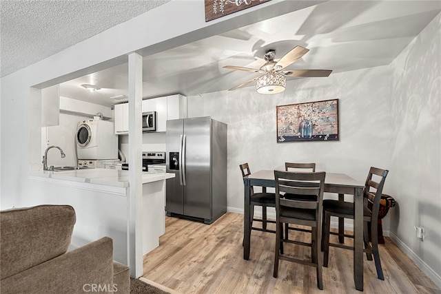 kitchen featuring appliances with stainless steel finishes, white cabinets, kitchen peninsula, stacked washer / drying machine, and ceiling fan