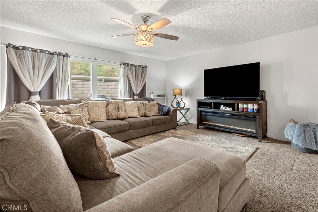 carpeted living room with ceiling fan and a textured ceiling