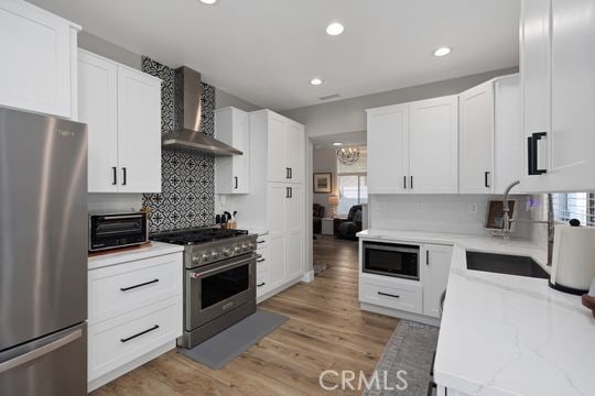 kitchen featuring appliances with stainless steel finishes, light hardwood / wood-style floors, white cabinetry, and wall chimney range hood