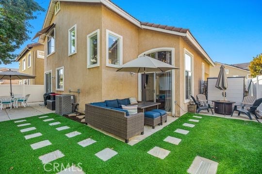 rear view of property featuring an outdoor living space with a fire pit, central air condition unit, a lawn, and a patio